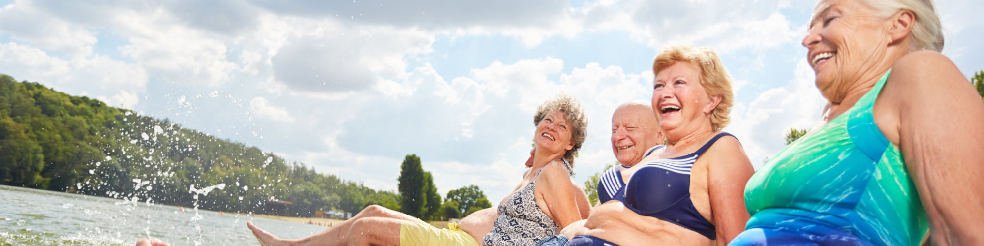 Active seniors splashing with their feet in the water during a summer vacation at the bathing lake